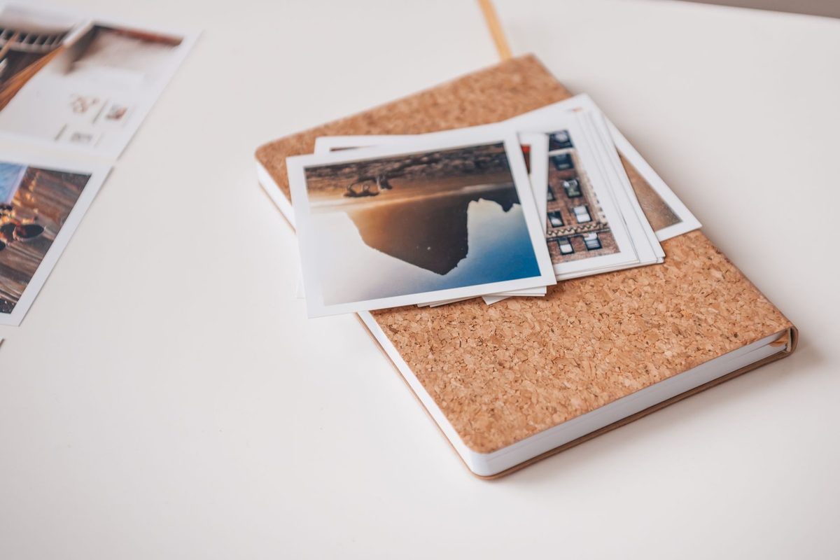Printed landscape photographs stacked on a cork-covered notebook on a white table