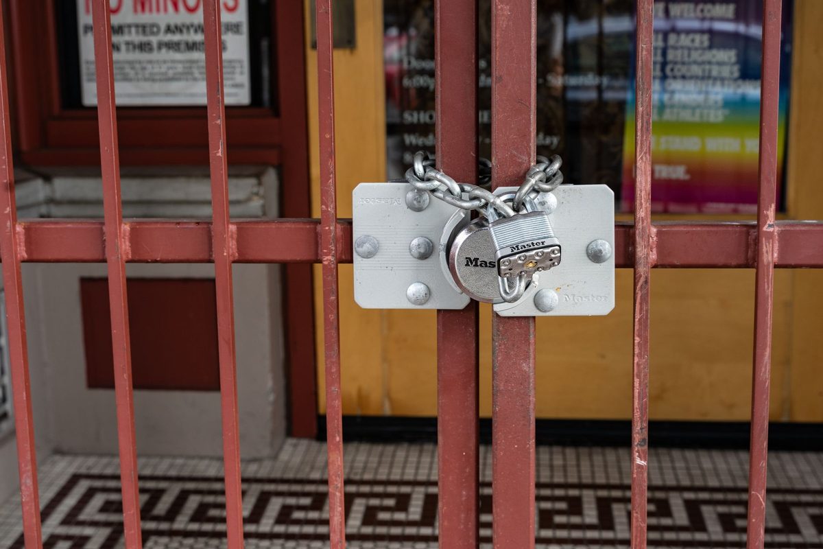 A silver padlock and chain fastening a red metal shop gate
